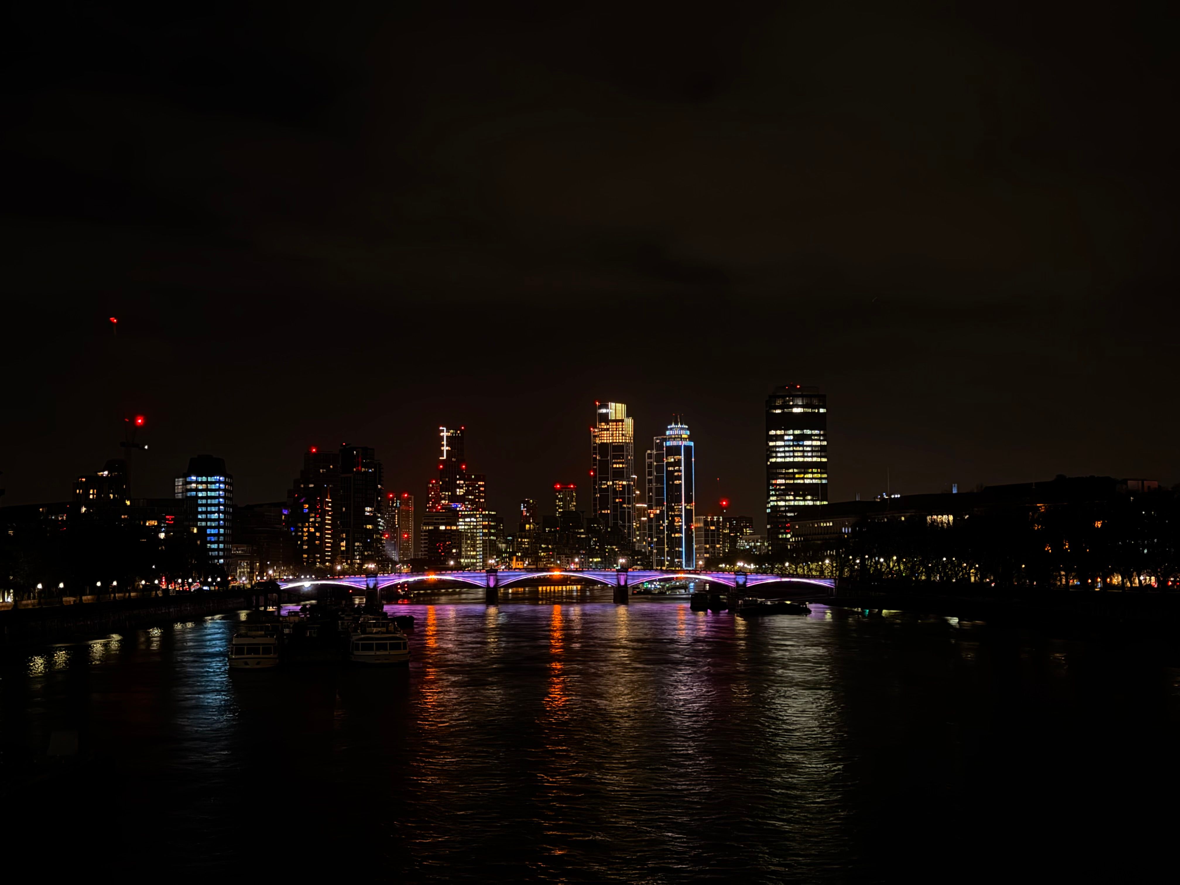 Illuminated London skyline and bridge reflected on the river at night.