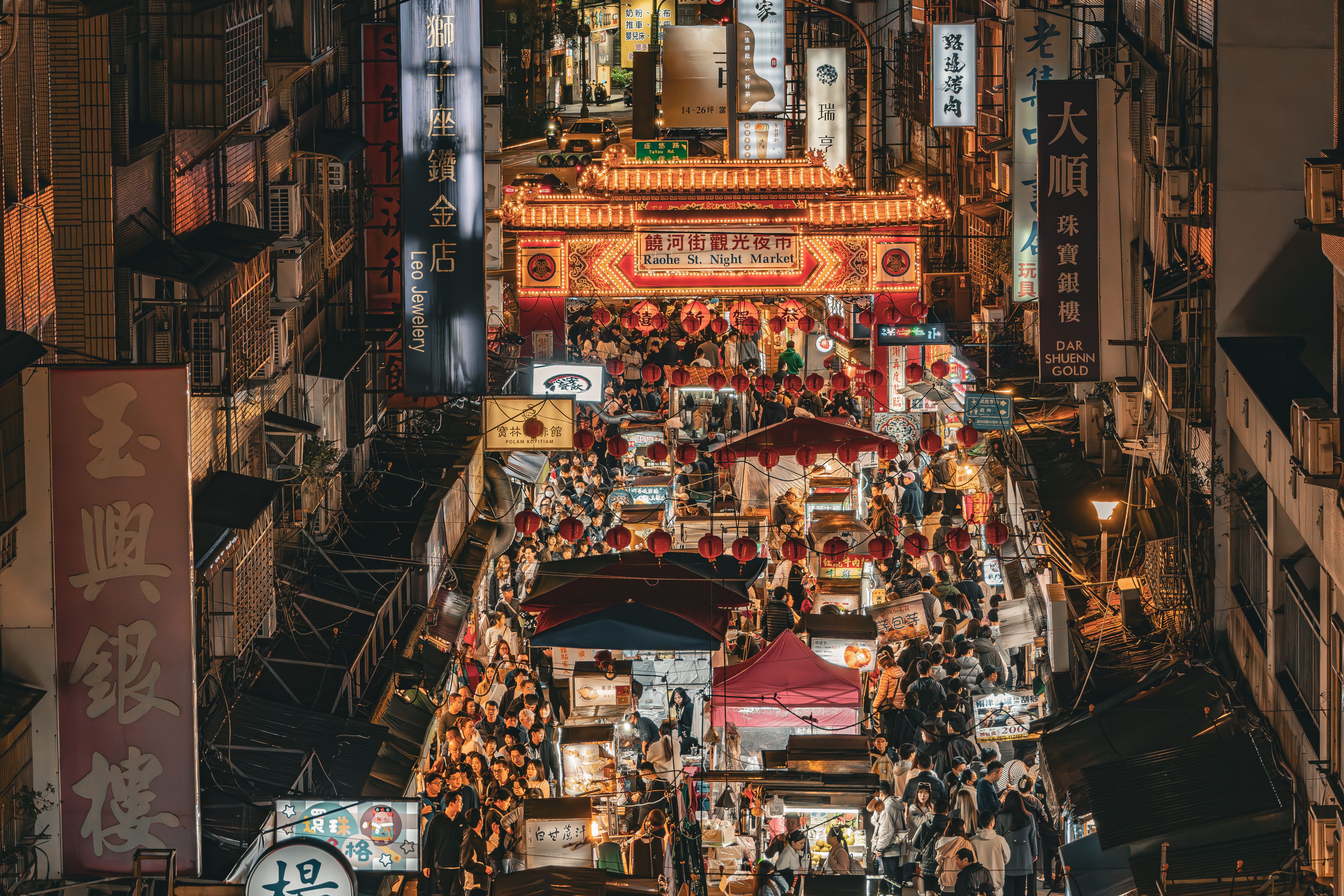Bustling Raohe Street night market in Taipei with illuminated food stalls and shoppers.